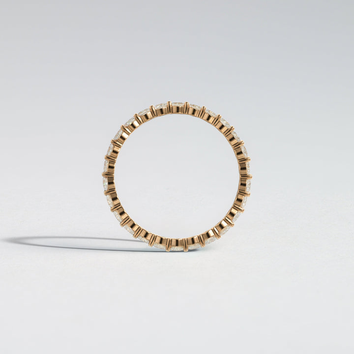 A delicate gold ring featuring a continuous row of small, bezel-set clear rectangular gemstones, photographed against a clean, light gray studio background #material_gold