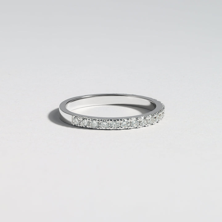 A thin silver band ring with a row of small clear pavé stones along the front, photographed on a clean light gray background #material_white