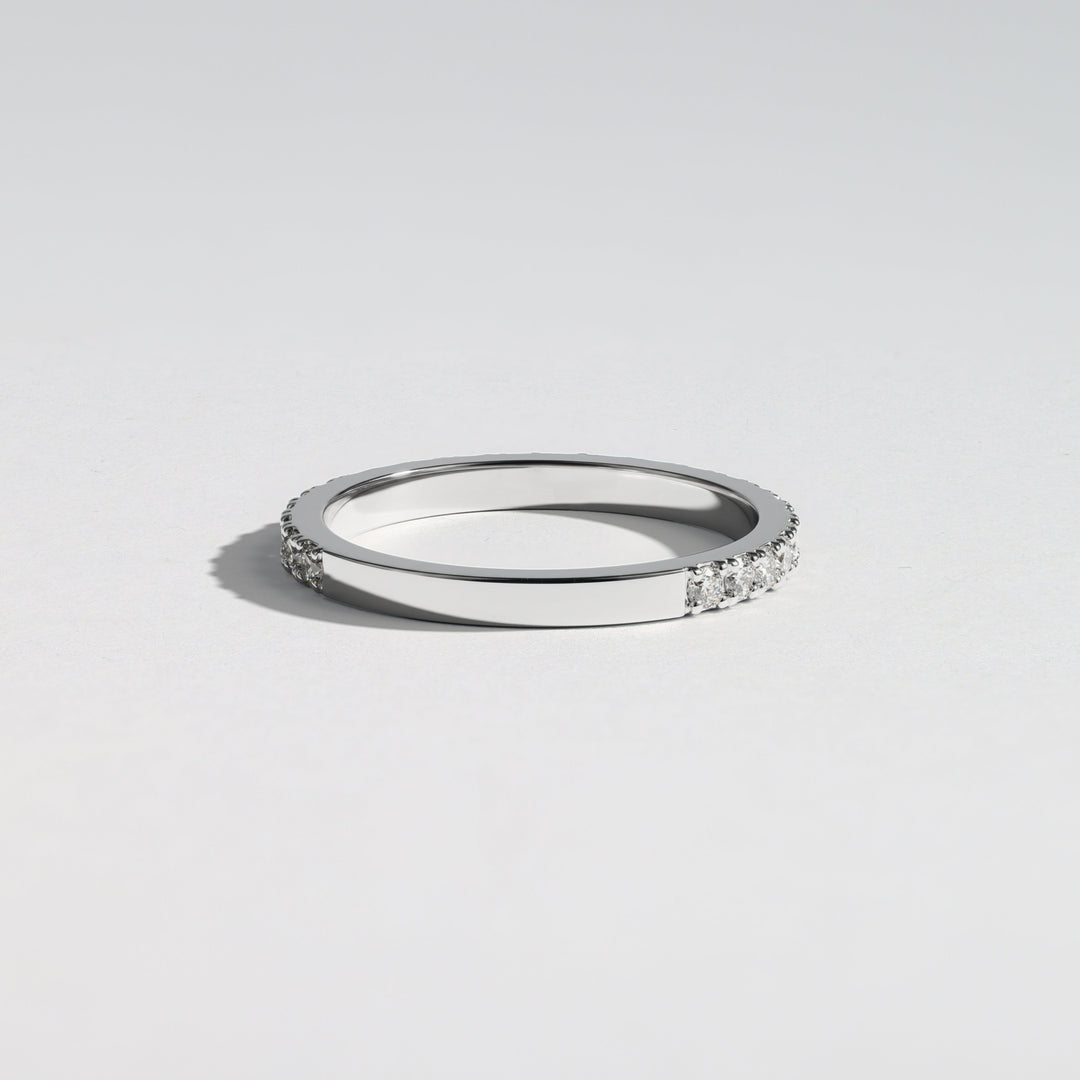 A slim silver band ring with a row of small clear stones on one side, photographed on a clean light gray background #material_white