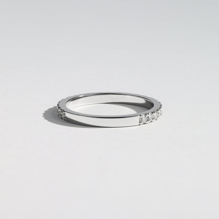 A slim silver band ring with a row of small clear stones on one side, photographed on a clean light gray background #material_white