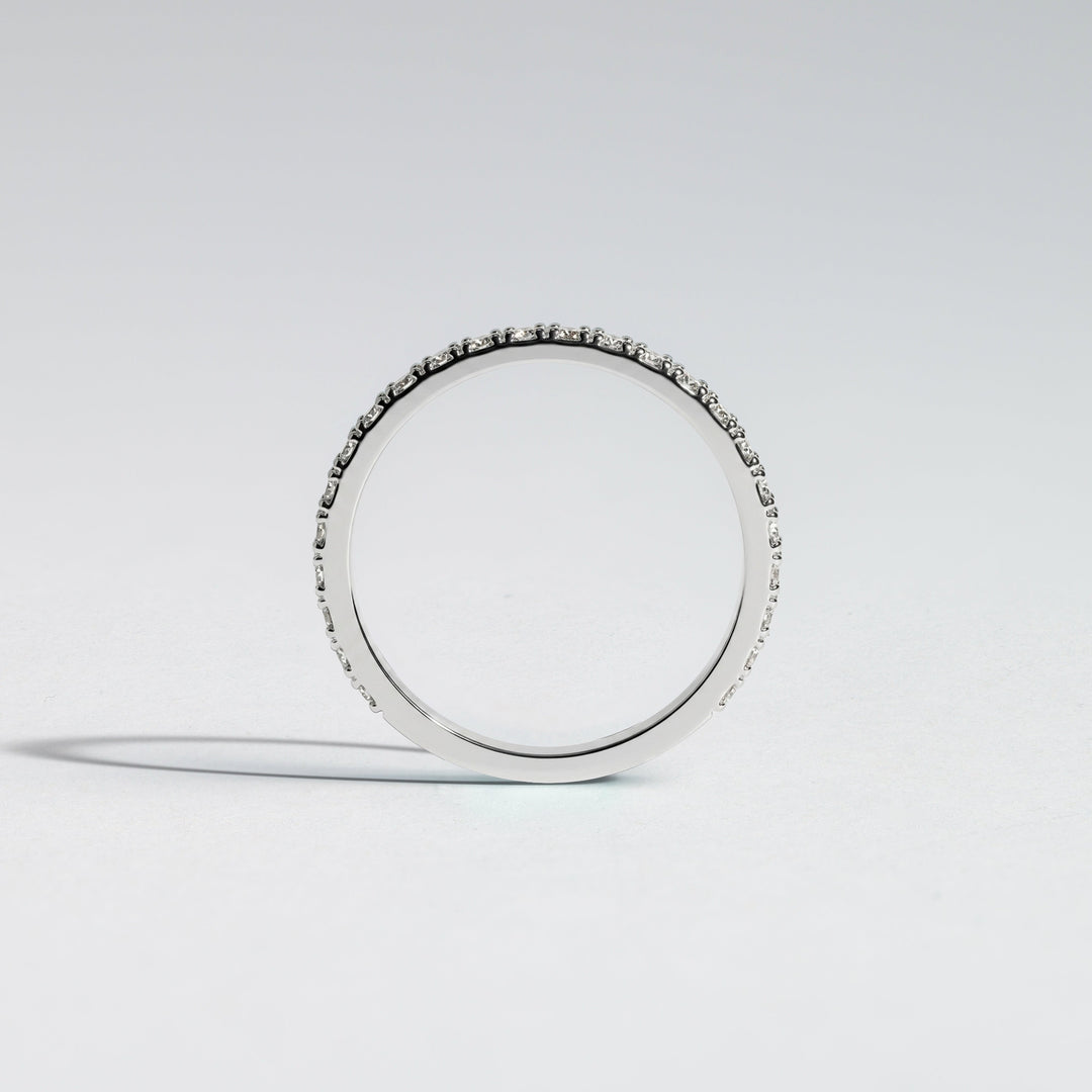A slim silver band ring with a row of small clear stones set along the outer edge, photographed on a clean light gray studio background #material_white