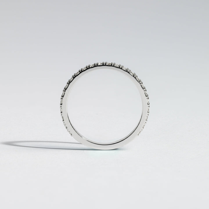 A slim silver band ring with a row of small clear stones set along the outer edge, photographed on a clean light gray studio background #material_white