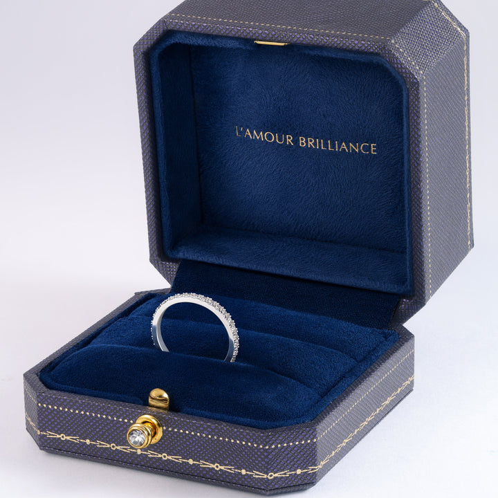 An open dark textured jewelry box with a deep blue velvet interior, displaying a gold ring with a small clear gemstone. The inside lid is lined with matching blue velvet and features the gold text 'L'AMOUR BRILLIANCE'. #material_white