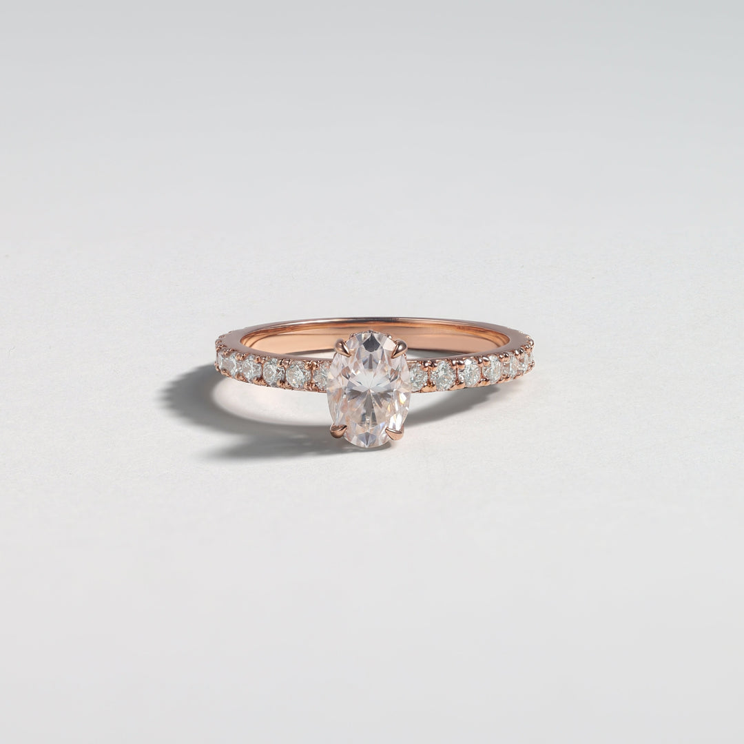 A rose gold ring with a central marquise-cut clear gemstone and pavé-set side stones, photographed on a clean light gray background #material_rose