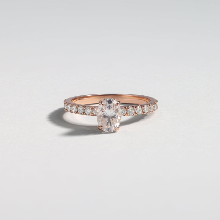A rose gold ring with a central marquise-cut clear gemstone and pavé-set side stones, photographed on a clean light gray background #material_rose