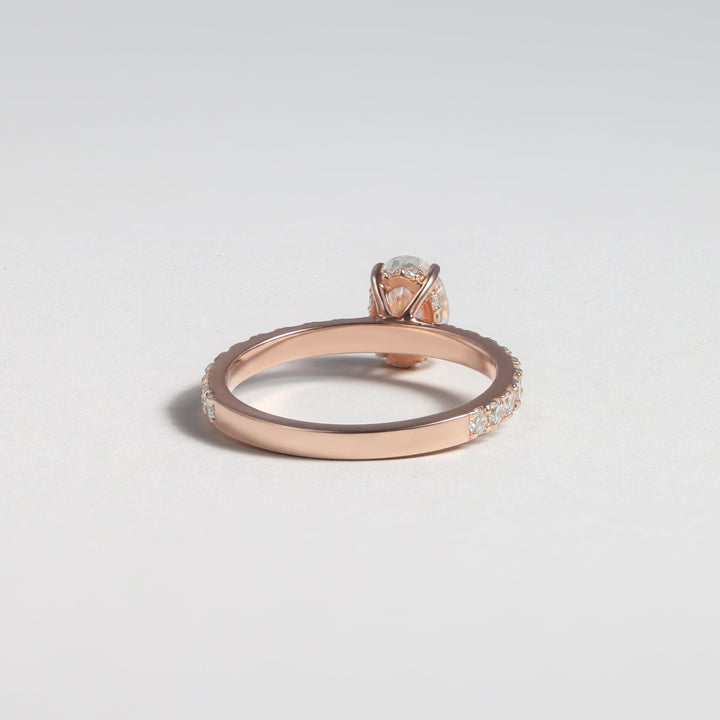 A rose gold ring with a small clear gemstone in a halo setting, shown on a light gray background #material_rose