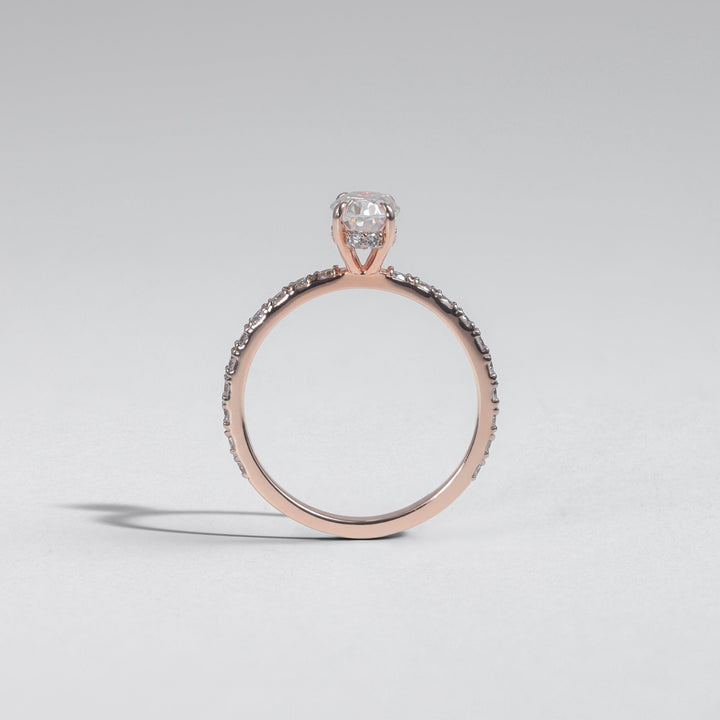 A rose gold ring with a single round-cut clear gemstone and a pavé band, photographed on a light gray background #material_rose