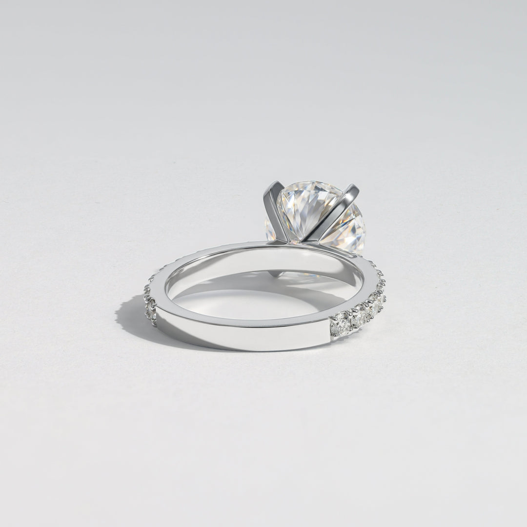 A silver-toned diamond ring with a large round-cut center stone and small pavé-set diamonds along the band, photographed on a clean light gray background #material_white