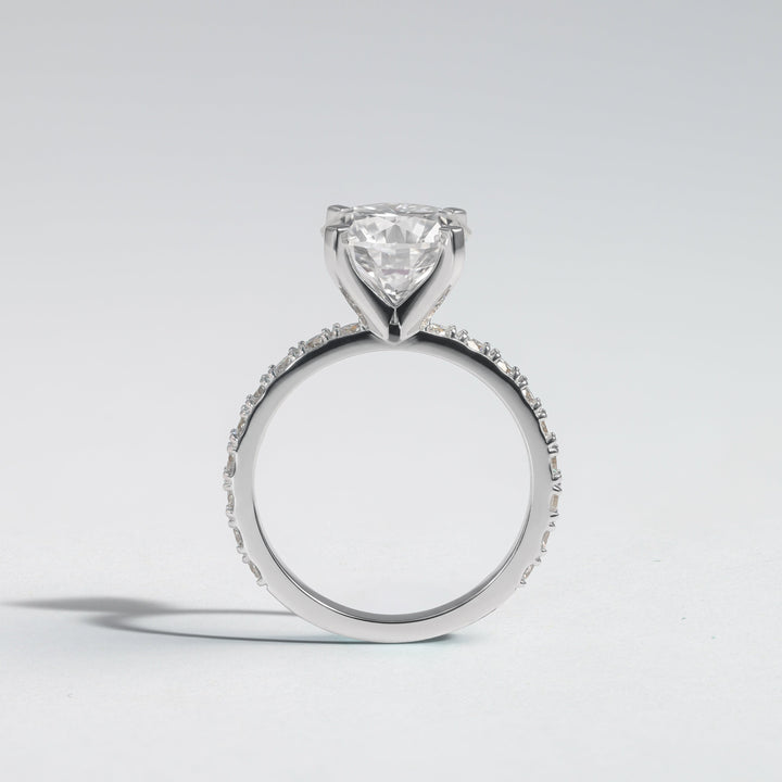 A silver-toned diamond ring featuring a heart-shaped clear gemstone in a prong setting, with a pavé band, shown on a light gray background  #material_white