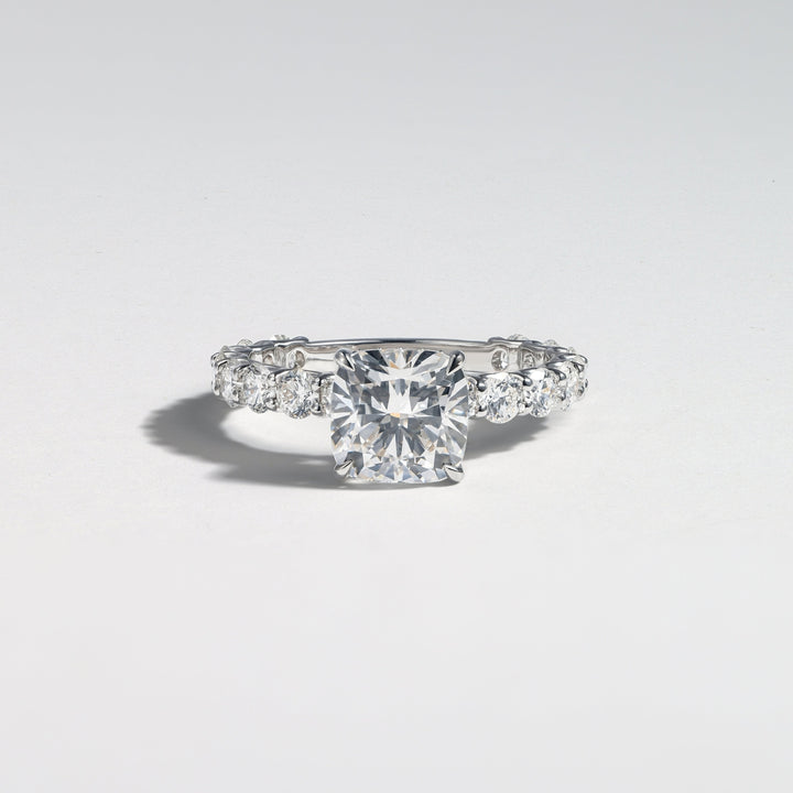 A silver-toned diamond ring featuring a prominent round-cut center stone and smaller diamonds along the band, photographed on a clean light gray background #material_white