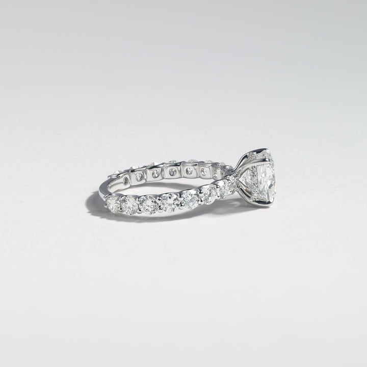 A silver-toned diamond eternity ring with a cushion-cut center stone and a continuous row of small diamonds along the band, photographed on a clean light gray background #material_white