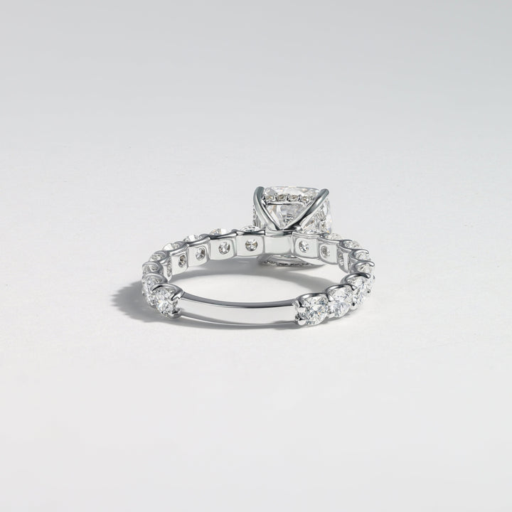 A silver-toned diamond ring featuring a rectangular cushion-cut center stone and a pavé band with small round diamonds, photographed on a light gray gradient background #material_white