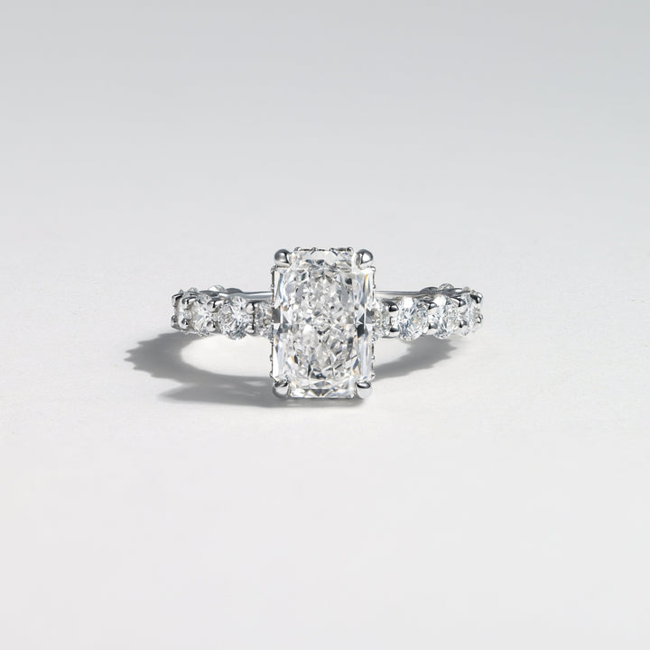 An emerald-cut diamond engagement ring with a silver-toned band featuring small side diamonds, photographed on a clean light gray background #material_white