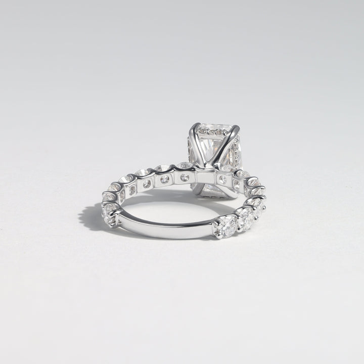 A silver-toned diamond ring featuring a rectangular emerald-cut center stone and a pavé band with small round diamonds, photographed on a light gray gradient background #material_white
