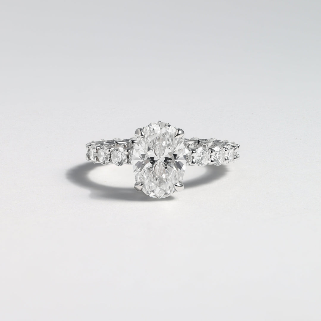 A silver diamond ring with a large oval-cut center stone and smaller diamonds along the band, photographed on a clean light gray background #material_white