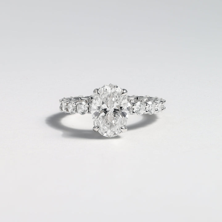 A silver diamond ring with a large oval-cut center stone and smaller diamonds along the band, photographed on a clean light gray background #material_white