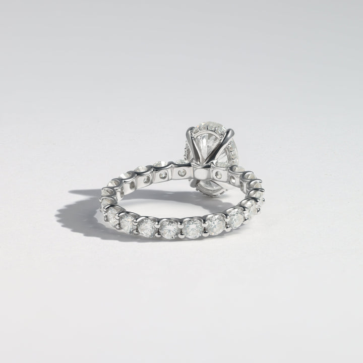 A silver-toned diamond ring with a brilliant oval-cut center stone and a continuous row of small diamonds along the band, photographed on a clean light gray background #material_white