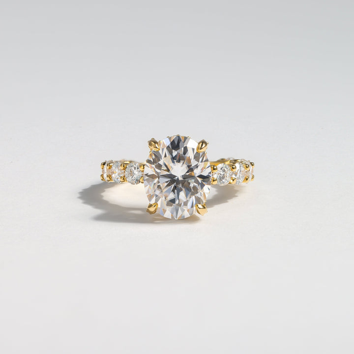 A yellow gold solitaire engagement ring with a round brilliant-cut center stone and a pavé band set with small round stones, photographed on a clean light gray background #material_gold
