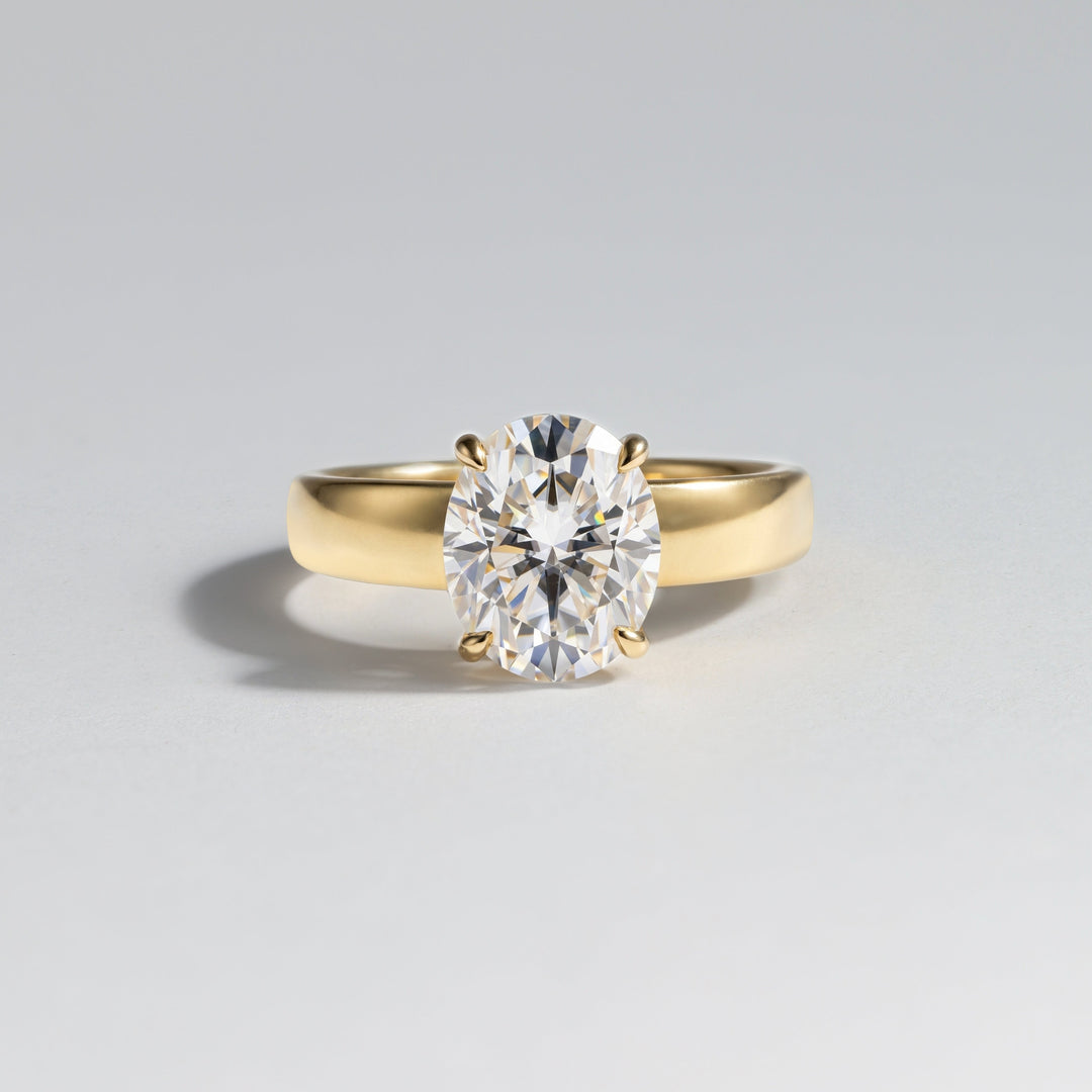 A yellow gold solitaire engagement ring featuring a round brilliant-cut diamond, photographed on a clean light gray background #material_gold