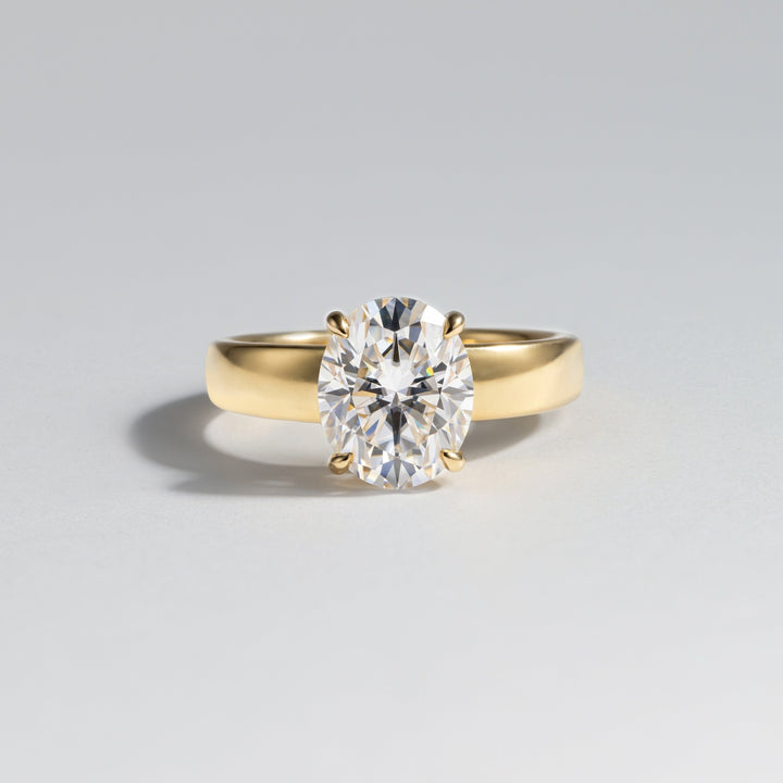A yellow gold solitaire engagement ring featuring a round brilliant-cut diamond, photographed on a clean light gray background #material_gold