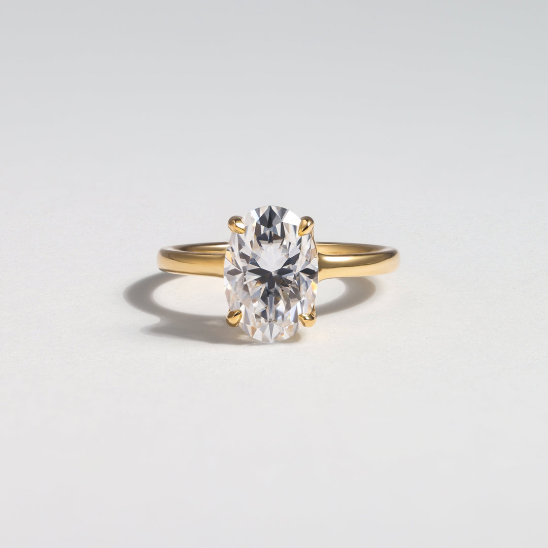 A yellow gold solitaire ring featuring a large oval-cut clear gemstone, photographed on a clean light gray background #material_gold