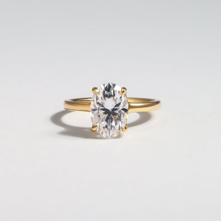 A yellow gold solitaire ring featuring a large oval-cut clear gemstone, photographed on a clean light gray background #material_gold