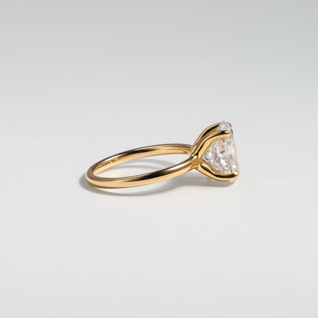 A gold ring with a triangular clear gemstone in a prong setting, photographed on a clean light gray background #material_gold