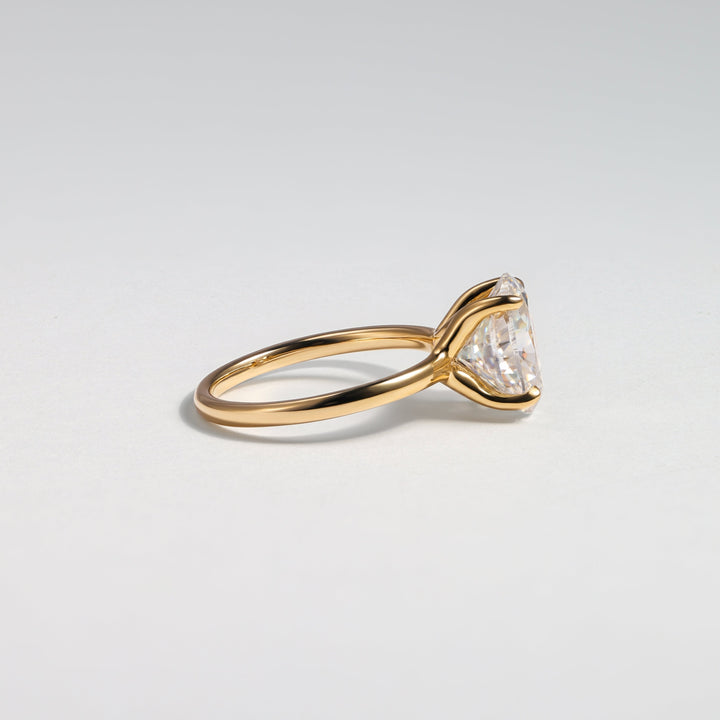 A gold ring with a triangular clear gemstone in a prong setting, photographed on a clean light gray background #material_gold