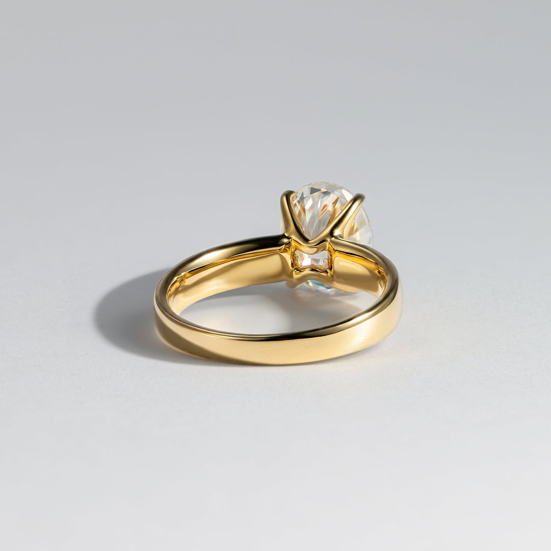 A yellow gold ring with a single clear gemstone in a prong setting, photographed on a clean light gray background #material_gold