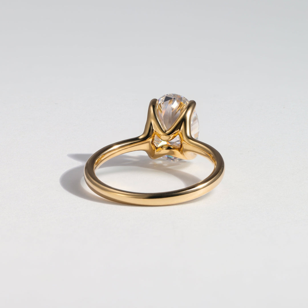 A gold ring with a pear-cut clear gemstone in a prong setting, photographed on a clean light gray background #material_gold