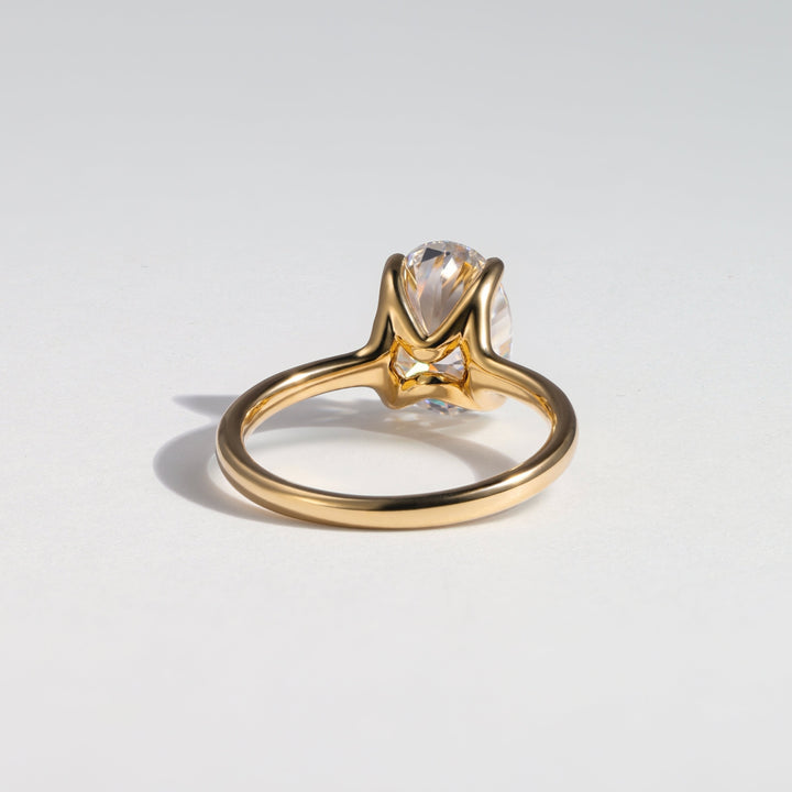 A gold ring with a pear-cut clear gemstone in a prong setting, photographed on a clean light gray background #material_gold