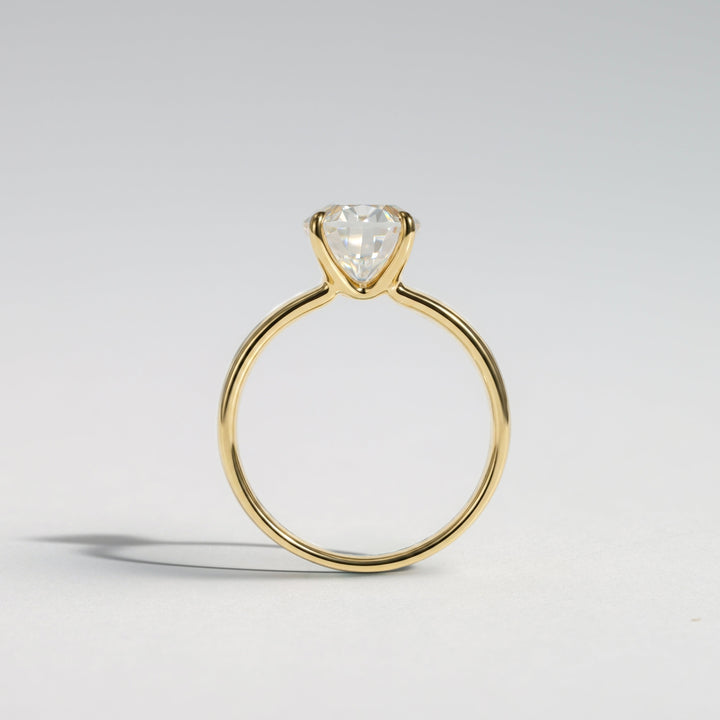 A yellow gold solitaire ring featuring a heart-shaped clear gemstone in a prong setting, photographed on a clean light gray background #material_gold