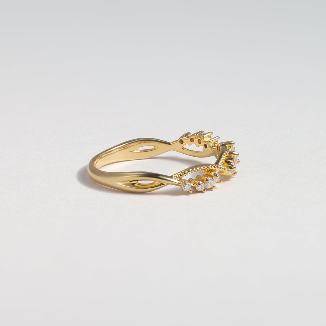 A gold ring with a twisted band and a small cluster of clear stones on the front, photographed on a clean light gray background #material_gold