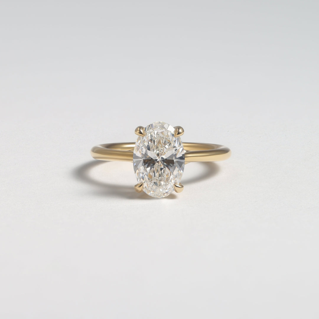 A yellow gold ring with a single oval-cut diamond set in a four-prong setting, photographed on a clean light gray background #material_gold