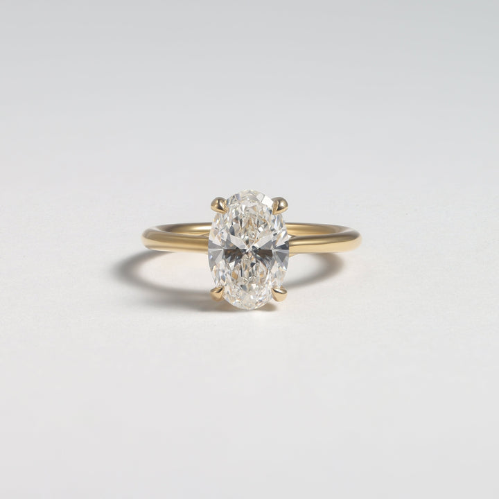 A yellow gold ring with a single oval-cut diamond set in a four-prong setting, photographed on a clean light gray background #material_gold