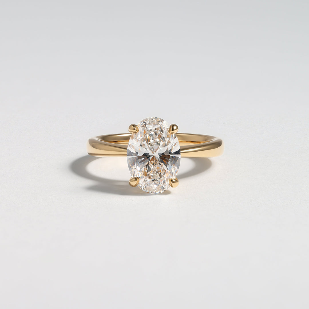 A yellow gold solitaire ring featuring a large oval-cut clear gemstone in a four-prong setting, photographed on a clean light gray background #material_gold