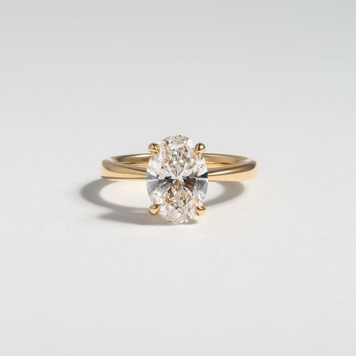 A yellow gold solitaire ring featuring a large oval-cut clear gemstone in a four-prong setting, photographed on a clean light gray background #material_gold
