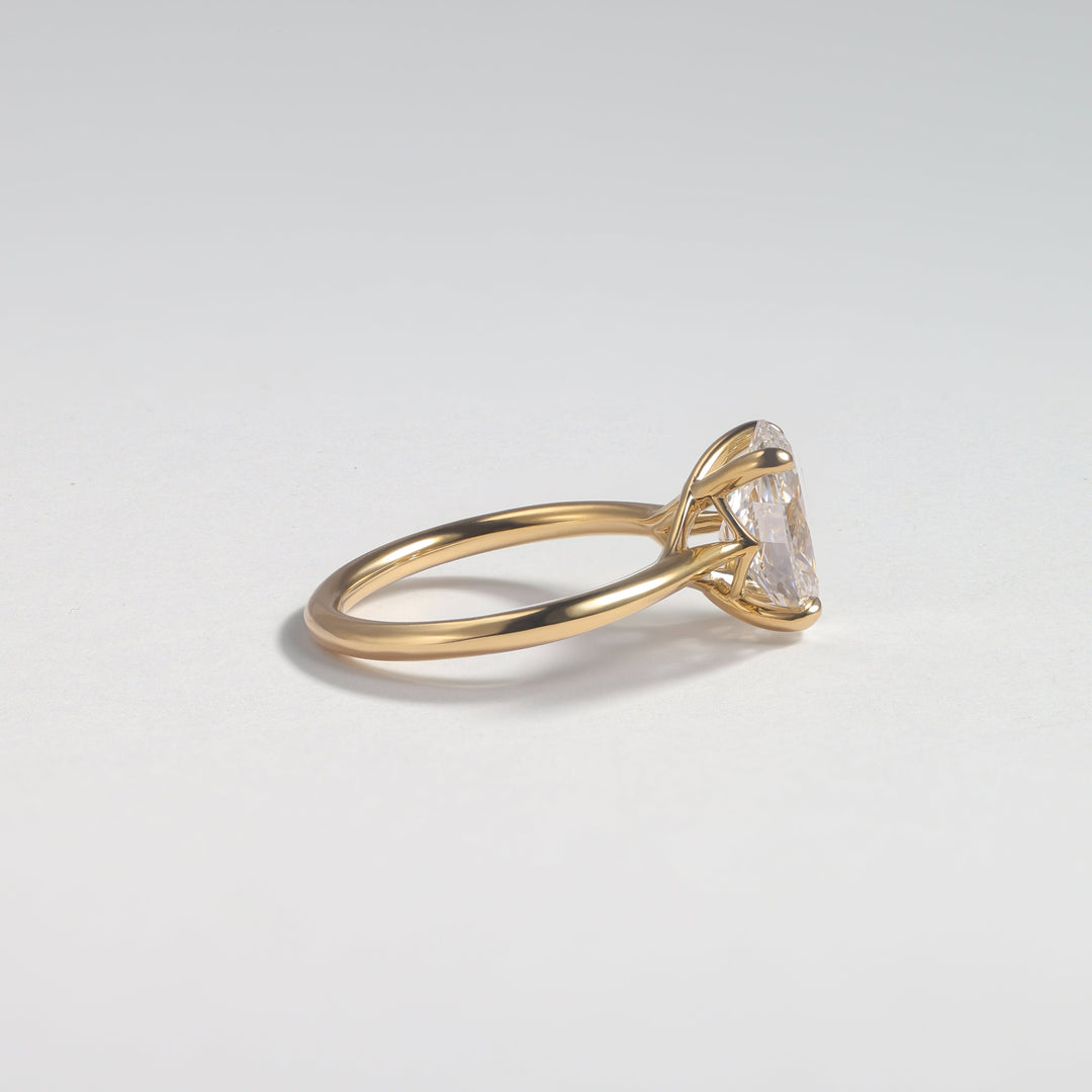 A gold ring with a triangular clear gemstone in a prong setting, photographed on a clean light gray background #material_gold