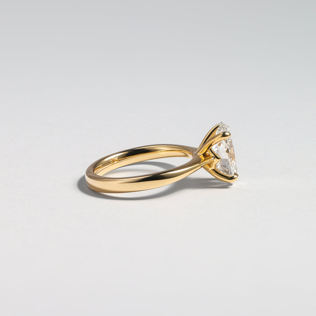 A gold ring with a triangular clear gemstone in a prong setting, shown from a side profile on a light gray background #material_gold