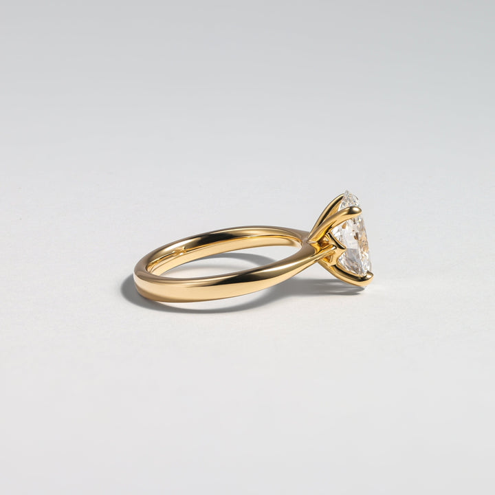 A gold ring with a triangular clear gemstone in a prong setting, shown from a side profile on a light gray background #material_gold