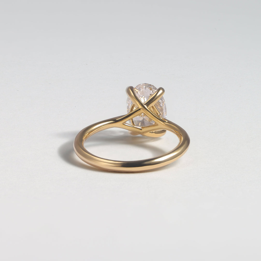 A gold ring with a twisted band and a clear, faceted gemstone in a prong setting, photographed on a light gray background #material_gold