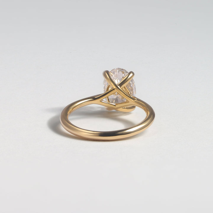 A gold ring with a twisted band and a clear, faceted gemstone in a prong setting, photographed on a light gray background #material_gold