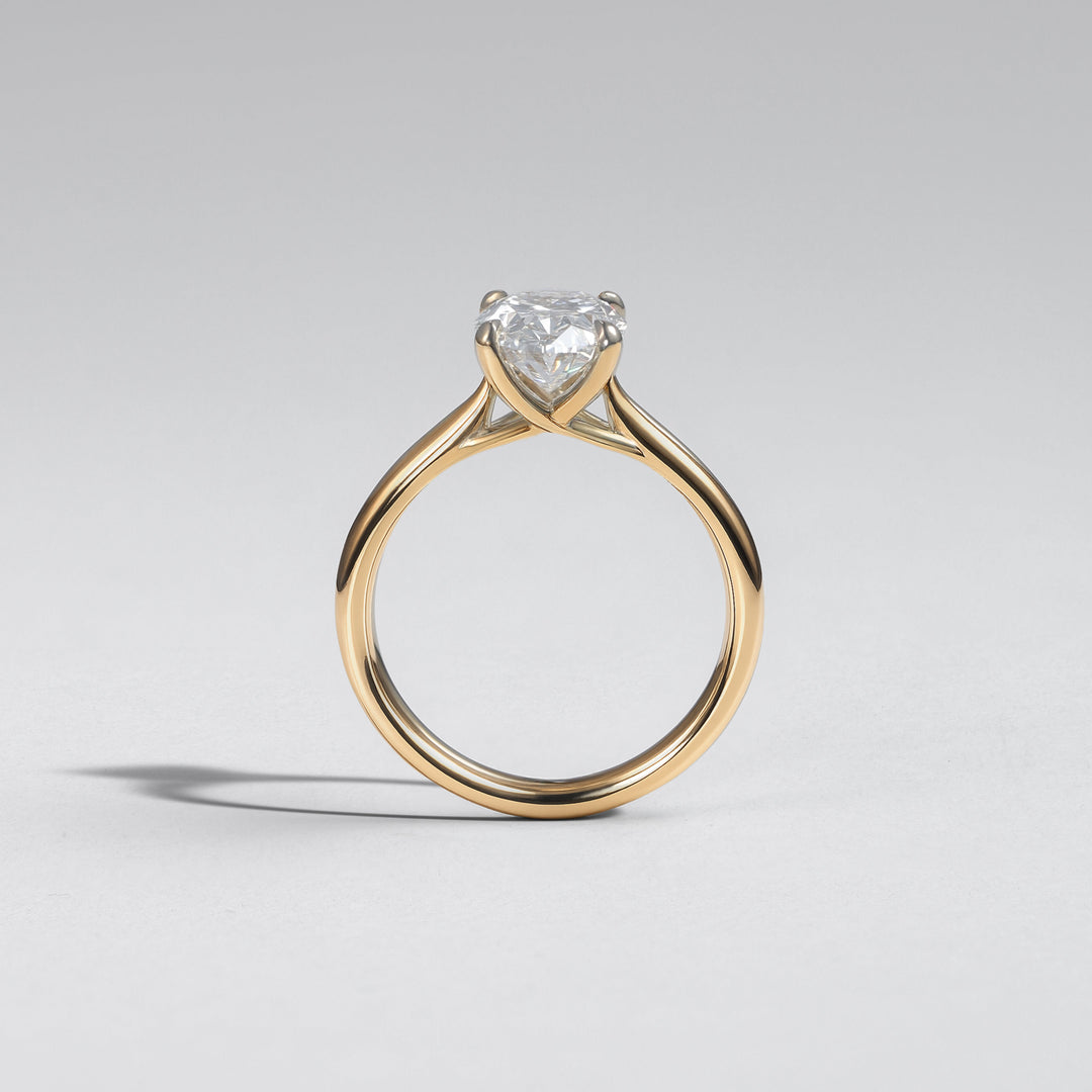 A yellow gold solitaire engagement ring featuring a heart-shaped clear gemstone, photographed on a neutral light gray background #material_gold
