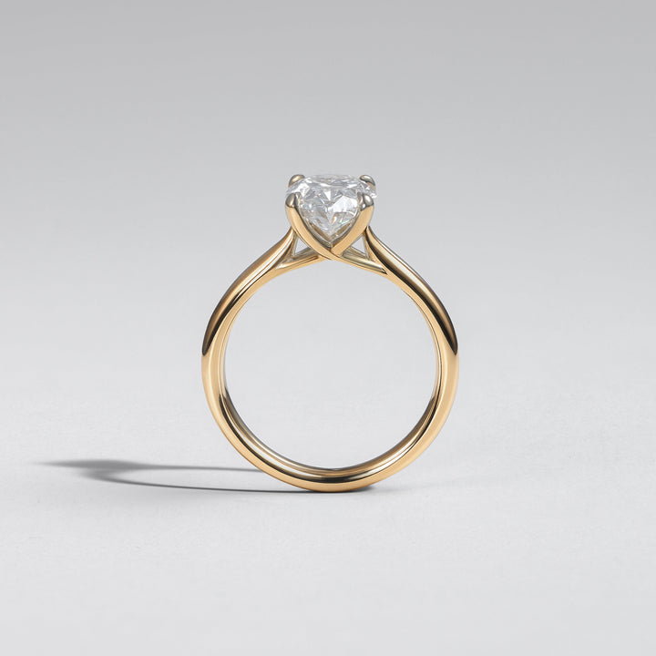A yellow gold solitaire engagement ring featuring a heart-shaped clear gemstone, photographed on a neutral light gray background #material_gold