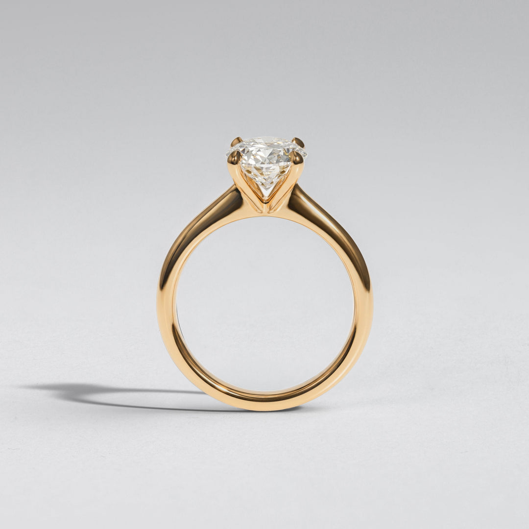 A yellow gold solitaire engagement ring with a heart-shaped clear gemstone, shown on a neutral light gray background #material_gold