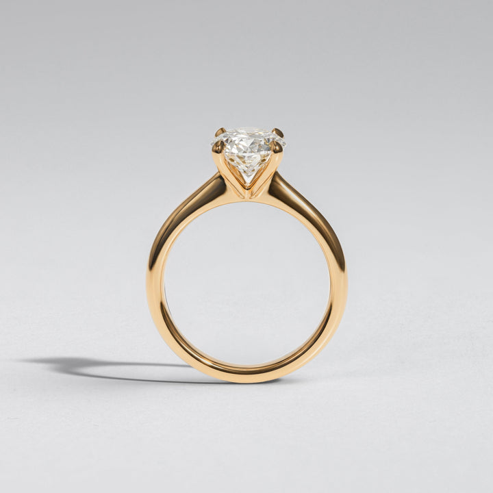 A yellow gold solitaire engagement ring with a heart-shaped clear gemstone, shown on a neutral light gray background #material_gold