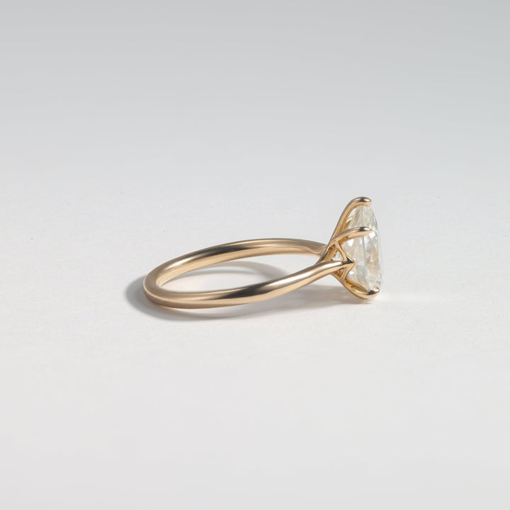 A gold ring with a marquise-cut clear gemstone in a prong setting, shown from a side profile view on a light gray background #material_gold