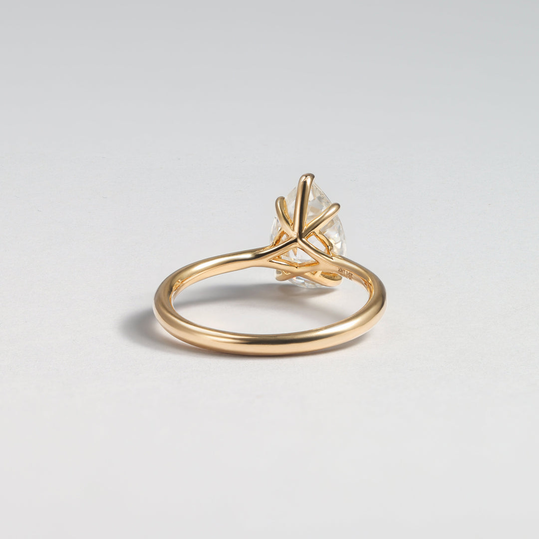 A gold ring with a unique twisted, crisscrossed band and a clear central gemstone, photographed on a neutral light gray background #material_gold