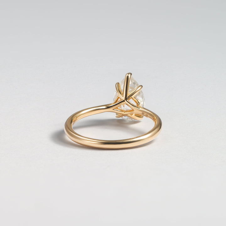 A gold ring with a unique twisted, crisscrossed band and a clear central gemstone, photographed on a neutral light gray background #material_gold