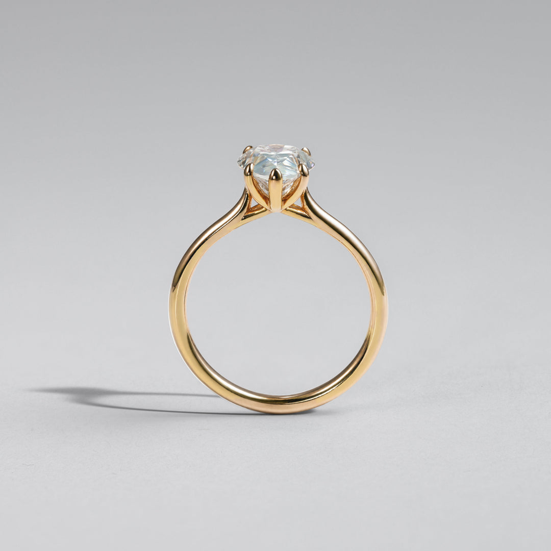 A yellow gold solitaire engagement ring with a round brilliant-cut clear gemstone, shown from the back on a neutral gray background #material_gold